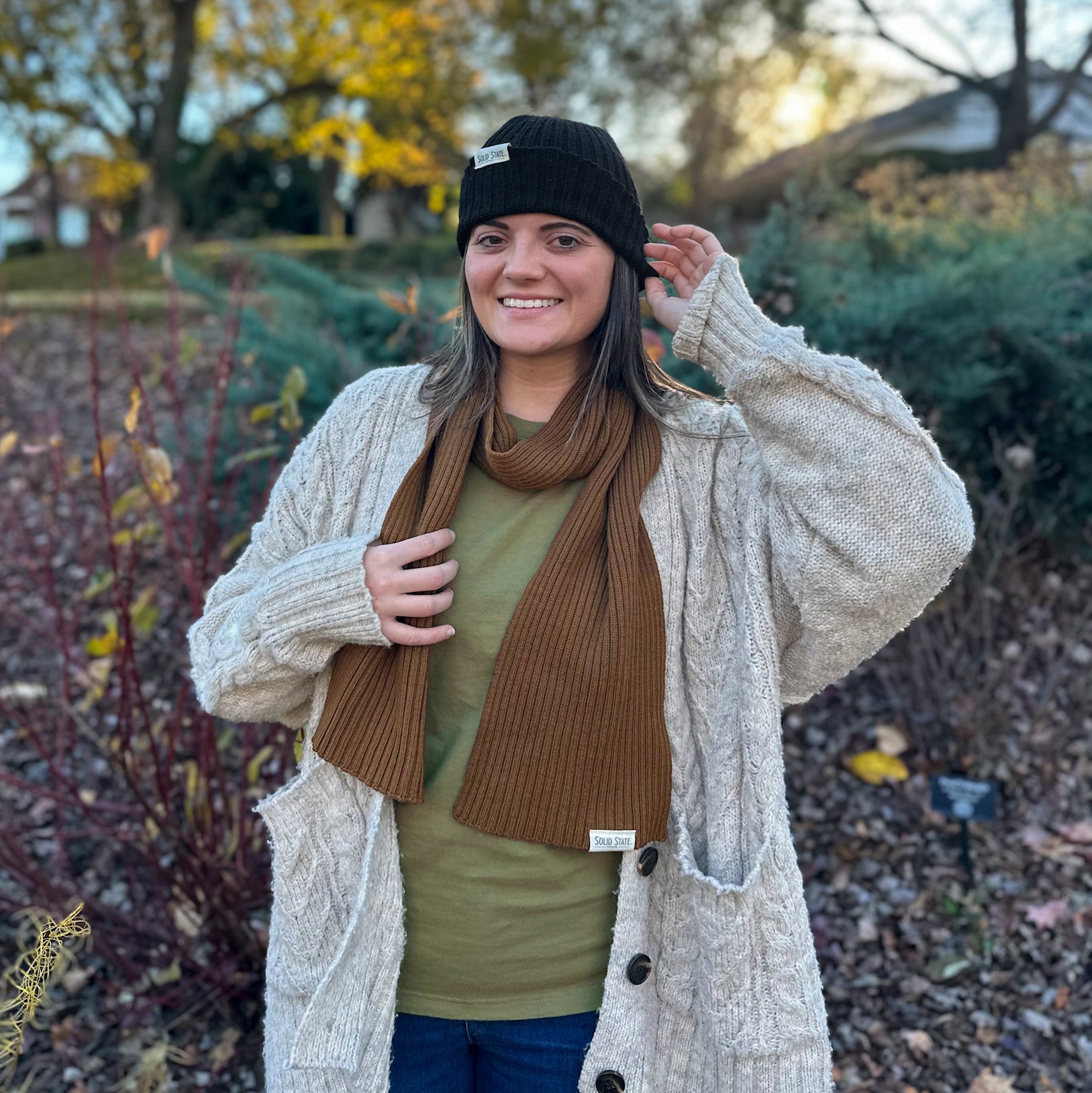 Woman wearing black beanie and brown scarf outdoors.