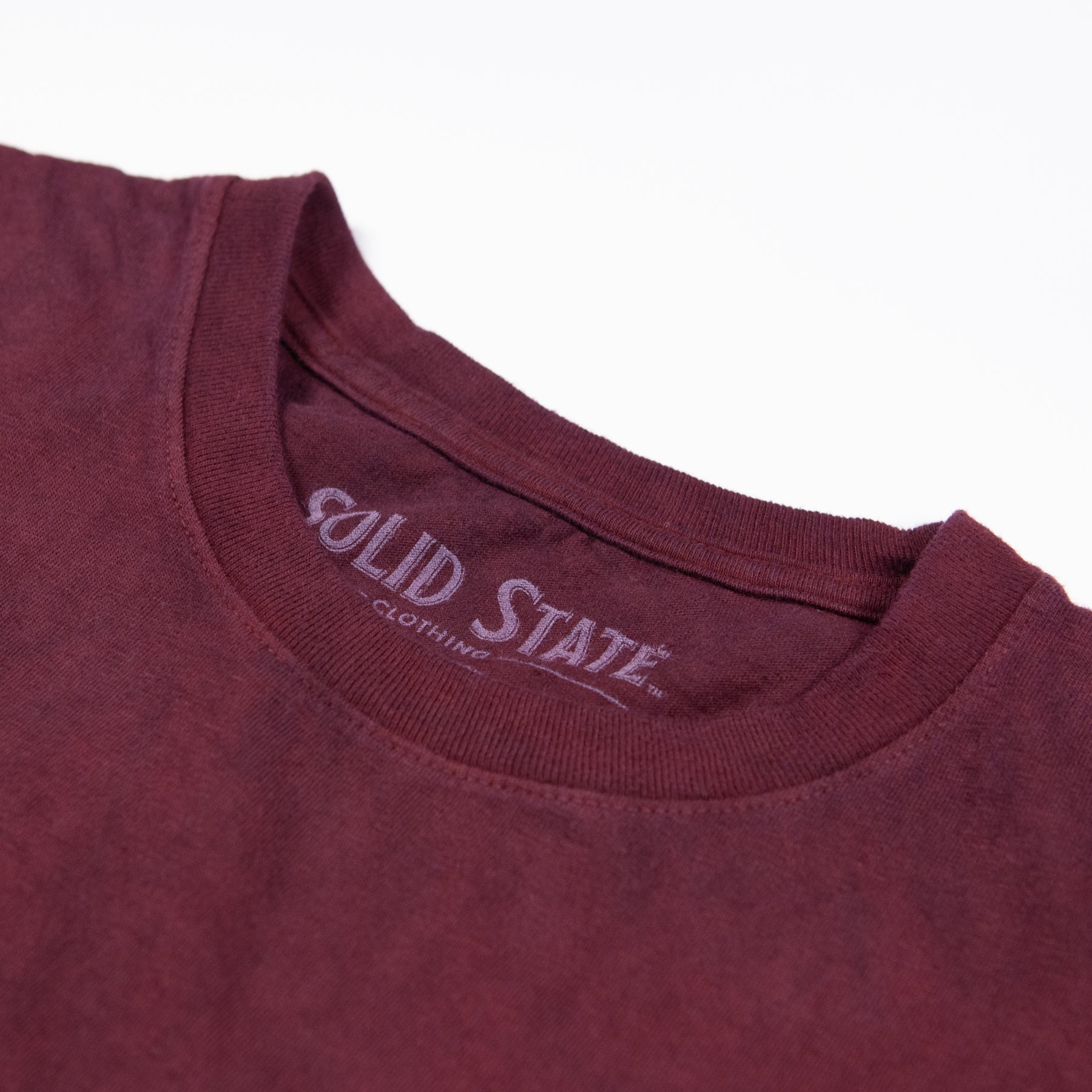 A close-up of the neckline of a crewneck t-shirt made in the USA and dyed with madder root standing laying flat on a white background. A label printed inside the neck reads "Solid State Clothing."
