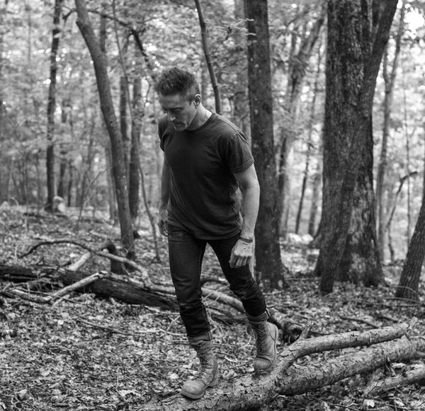 A black and white photo of a man hiking in the woods while wearing a Solid State Clothing Homesteader Fit M t-shirt