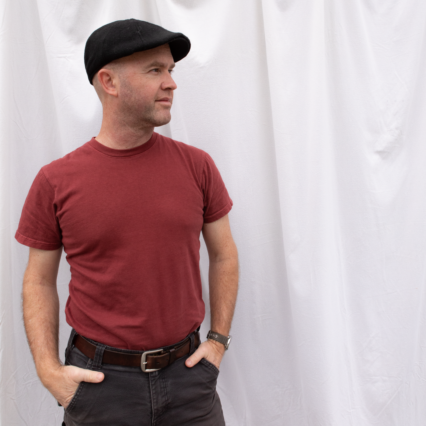 A man, wearing an American-made Solid State Clothing Natural Dye Shirt in Port, looks off into the distance. He is standing in front of a white background