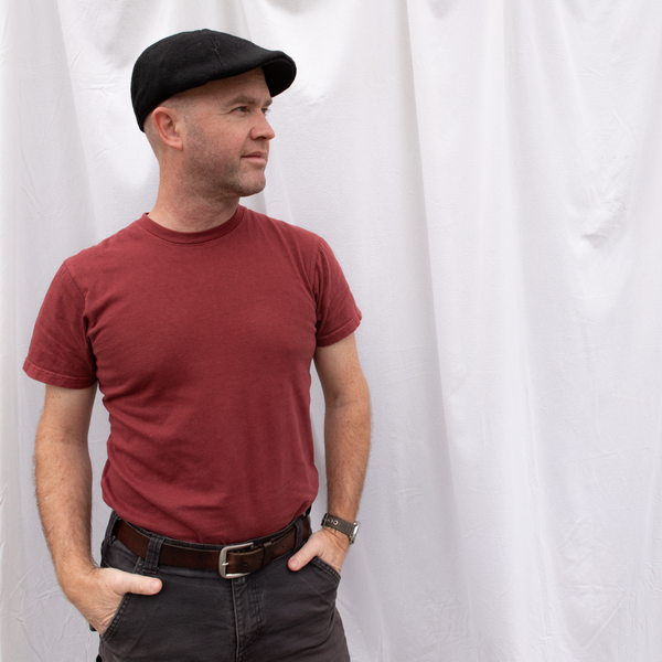 A man, wearing an American-made Solid State Clothing Natural Dye Shirt in Port, looks off into the distance. He is standing in front of a white background