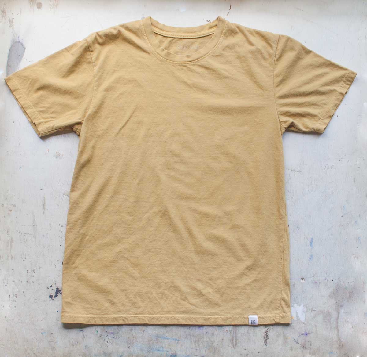 A Solid State Clothing Natural Dye t-shirt lies against a white background. The color of the shirt is Citrine, which is a darker, muted shade of yellow