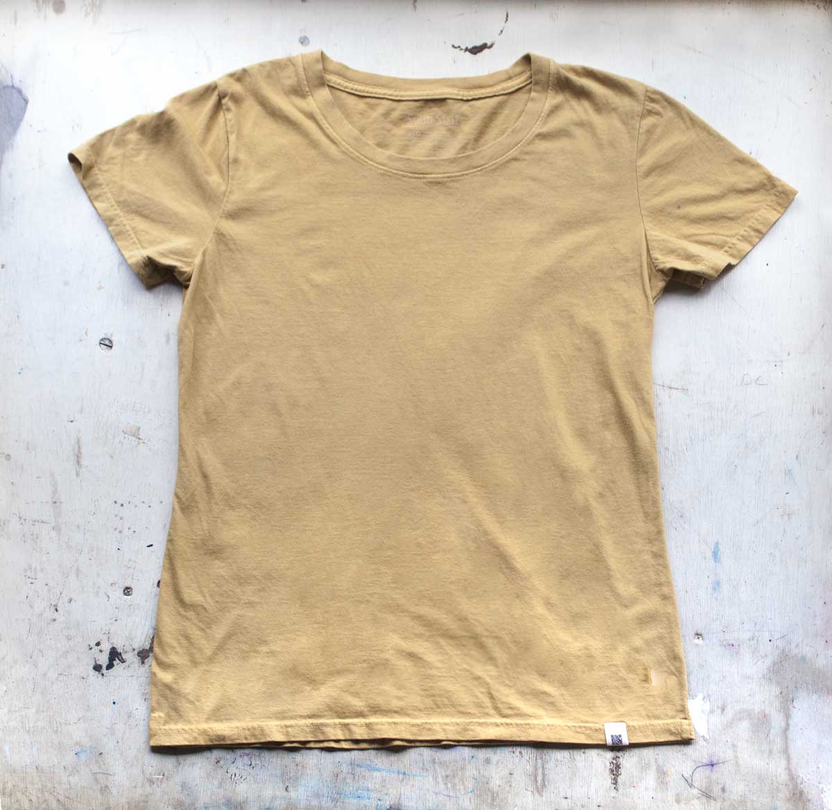 A Solid State Clothing Natural Dye t-shirt lies against a white background. The color of the shirt is Citrine, which is a darker, muted shade of yellow